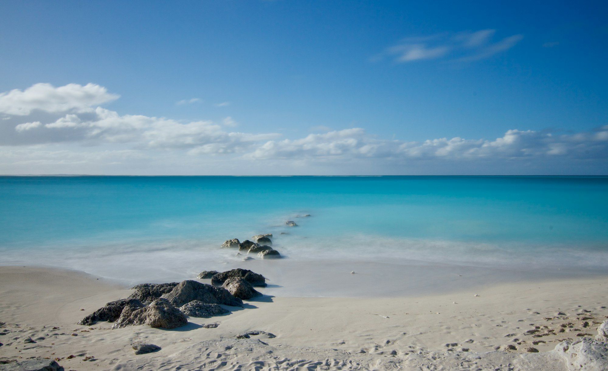 Turquoise water and a white sand beach with a line of rocks in the Turks and Caicos Islands